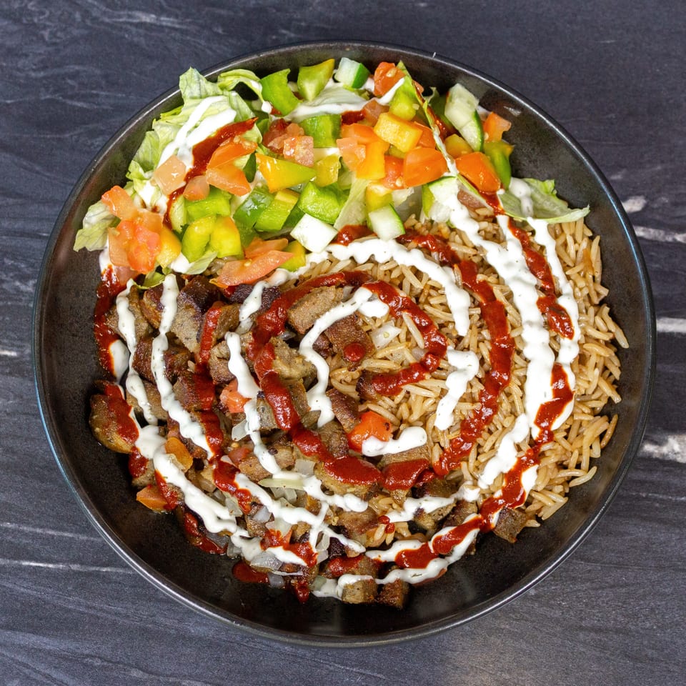Bowl of seasoned rice topped with grilled meat, lettuce, diced tomatoes, peppers, and white and red sauces.