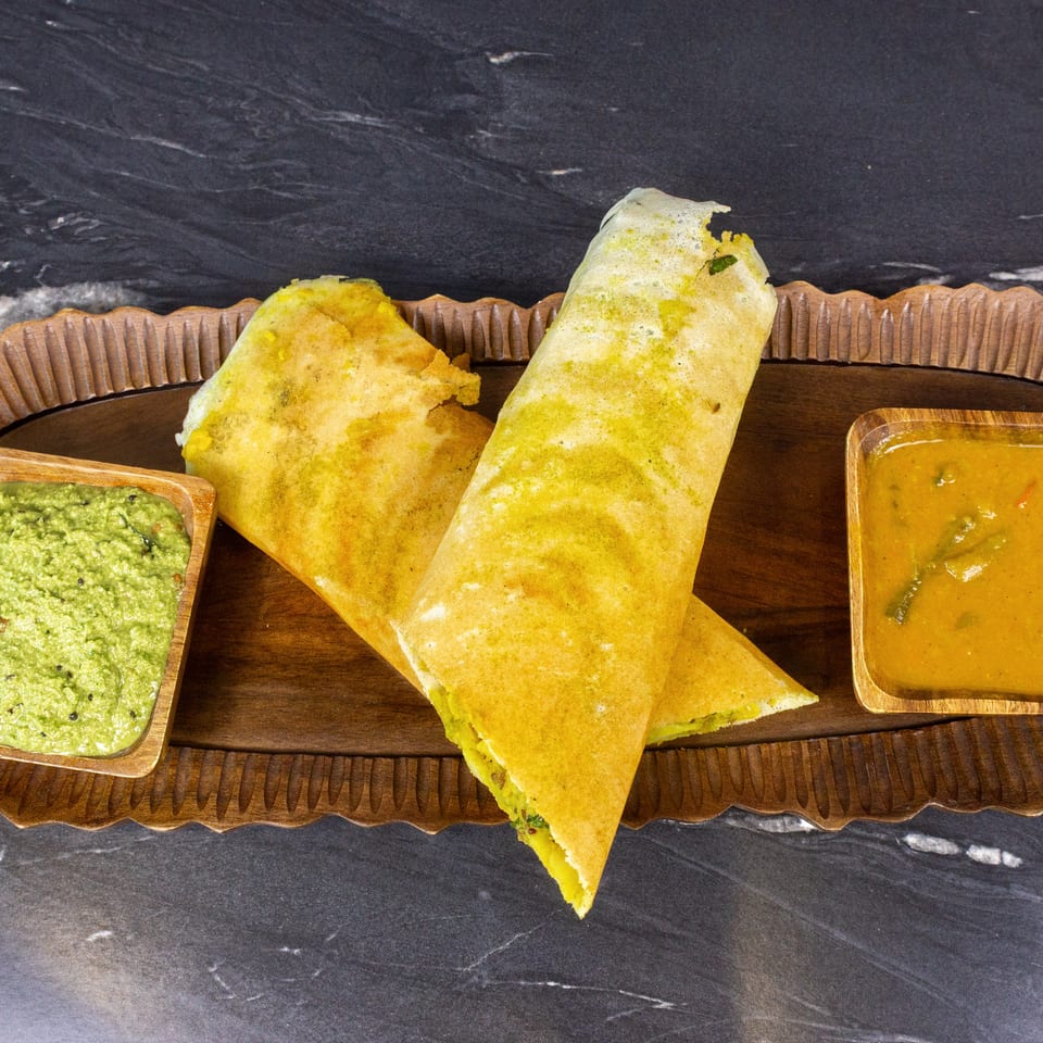 Crispy folded dosa served on a wooden platter with green coconut chutney and orange sambar.