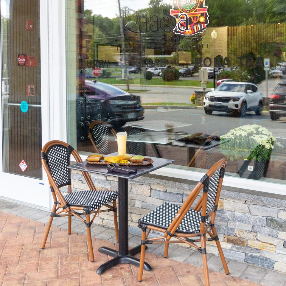 Raad Express Indian restaurant storefront with outdoor café seating, sandwiches, a drink, and colorful signage on the window.
