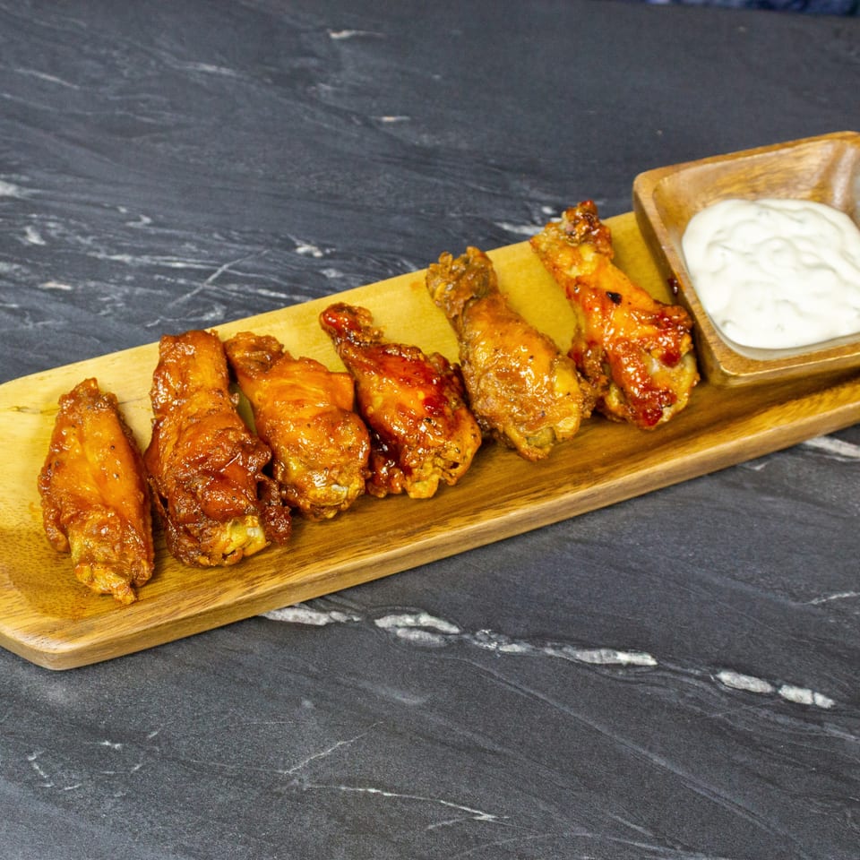 Glazed chicken wings arranged on a wooden serving board with creamy dipping sauce on a dark marble table.