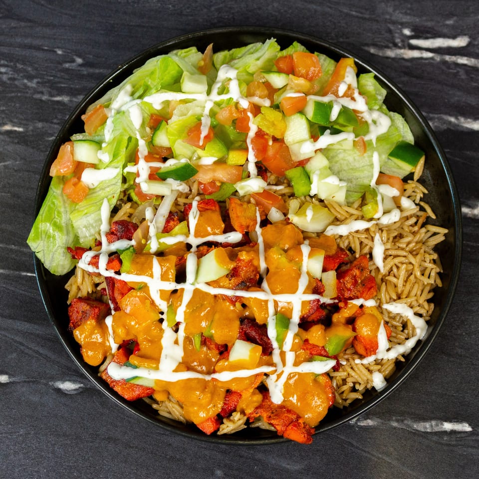 Loaded bowl of seasoned rice, grilled chicken, lettuce, tomatoes, cucumbers, peppers, and orange and white sauces.