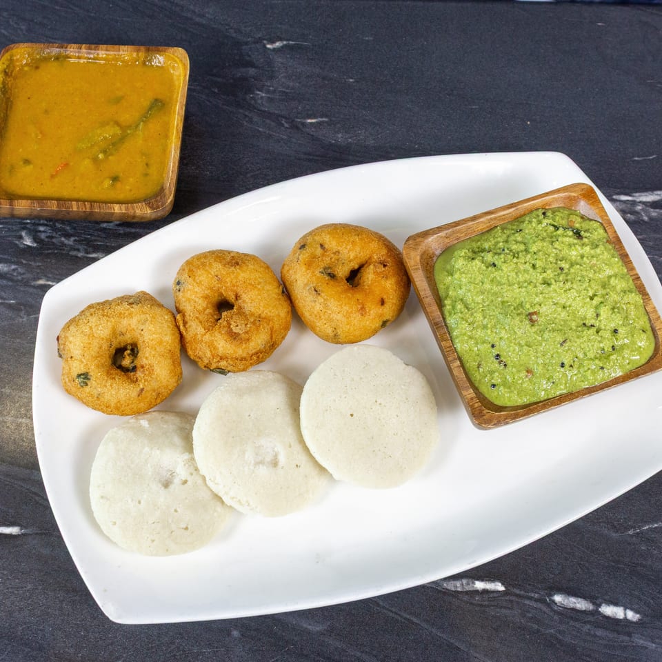 South Indian breakfast platter with idlis, vadas, green coconut chutney, and sambar on a white plate.