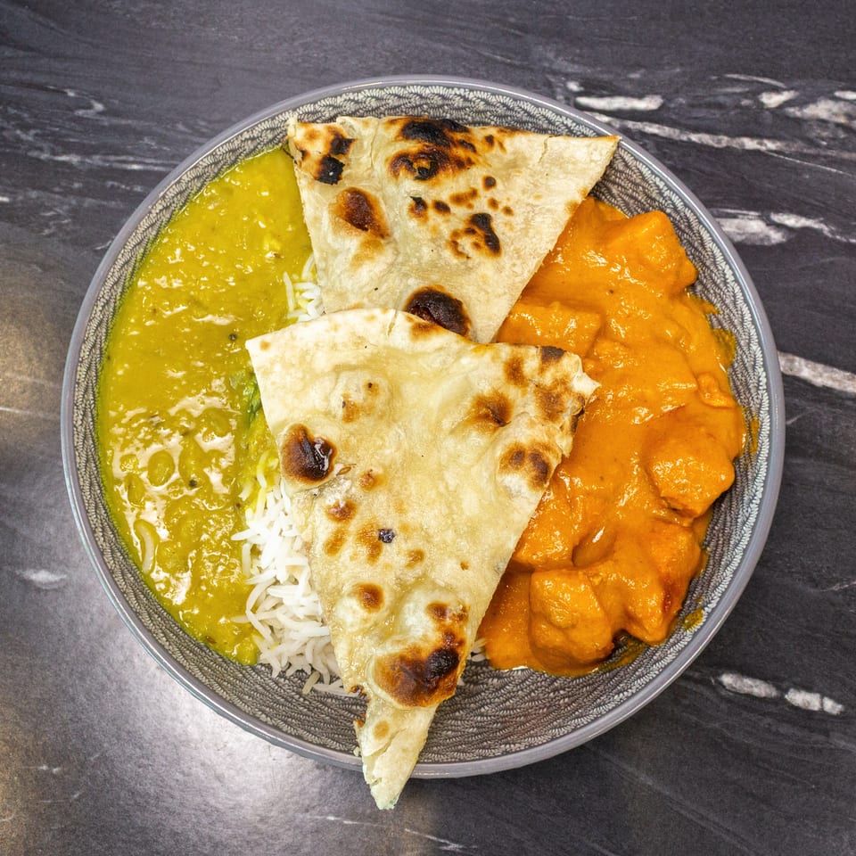 Overhead view of naan bread, white rice, and green and orange curries served on a patterned plate.