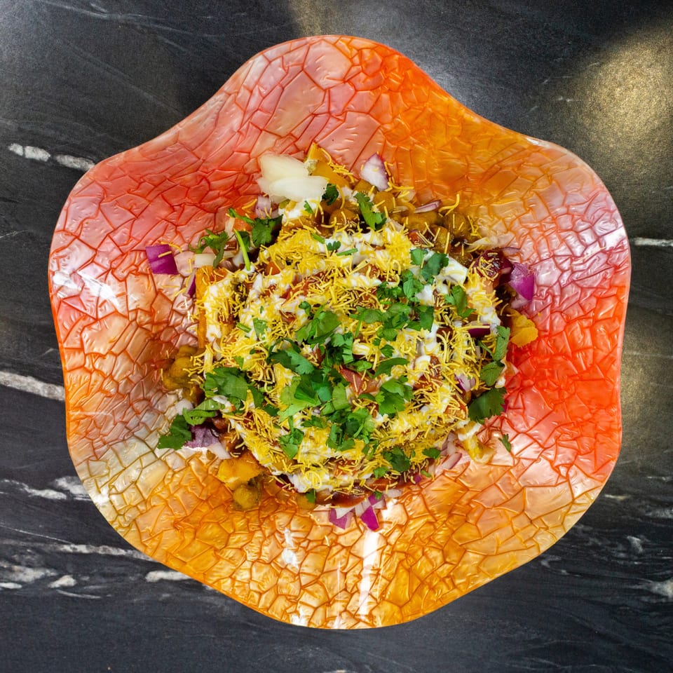 Indian chaat topped with sev, yogurt, chutneys, chopped onions, and fresh cilantro on an orange textured plate.