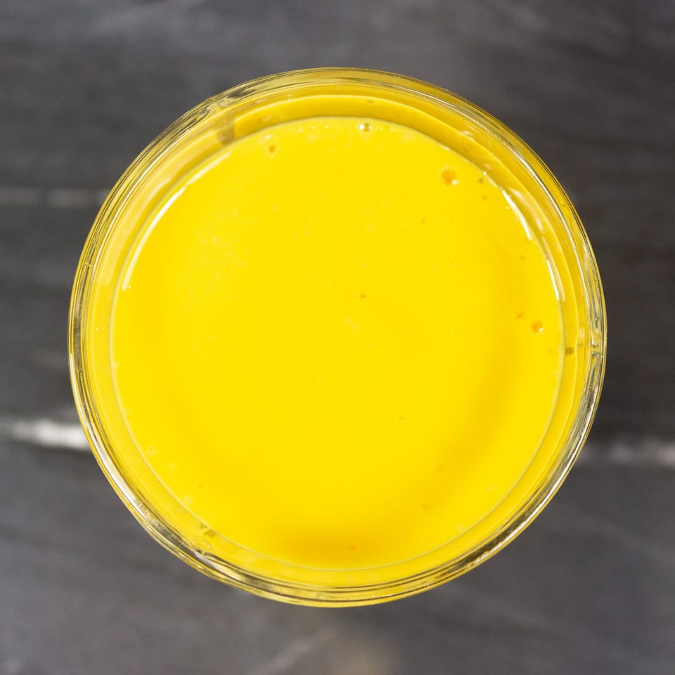 Top-down view of a glass bowl filled with smooth, bright yellow sauce on a dark surface.